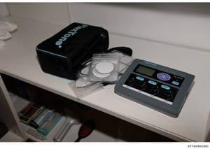 This photograph shows a white shelf or counter displaying professional facial analysis or skin analysis equipment, including a FitaFlone RX-8000 device with digital controls, optical measurement probes in a clear storage case, and a black carrying ca