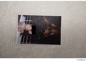 This is an evidence photograph containing a printed image placed on a light-colored surface. The photograph shows a partially visible scene with significant redaction (black bar) obscuring the central content. The left side shows what appears to be h