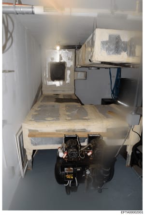 This is a photograph of a confined underground space containing HVAC/mechanical equipment, electrical systems, and storage. The room appears to show a basement or sub-level utility area with exposed wiring, ductwork, and what appears to be a furnace 