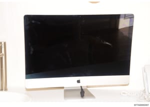 This is a photograph of an Apple iMac computer with a white bezel and aluminum stand, displaying a black screen. The photo appears to be evidence documentation from the Epstein investigation, likely seized during property searches. The computer's con