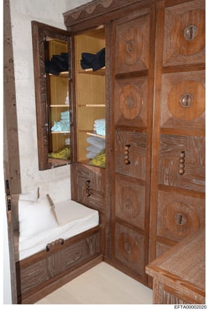 This photograph shows a wooden bathroom cabinet or wardrobe with mirrored glass doors and decorative circular inlays. The cabinet contains stacked towels and linens in white, light blue, and yellow colors. The image appears to be an interior document