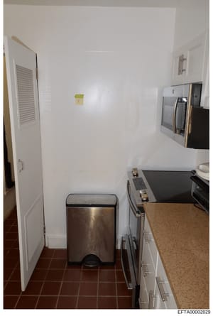 This is a photograph of a residential kitchen interior, showing appliances, countertops, and storage areas. The image appears to be evidence documentation from a property inspection related to the investigation, with a Bates stamp indicating it is pa
