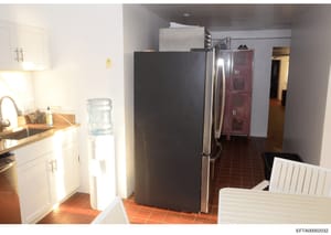 This is a color photograph of a residential kitchen interior, showing white cabinetry, stainless steel appliances, dark tile flooring, and various storage elements. The image appears to be evidence documentation from the Epstein investigation, likely