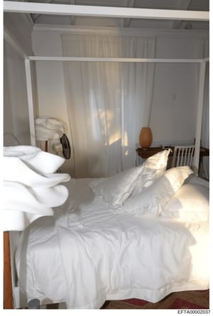 This is a photograph of a bedroom interior featuring a four-poster bed with white linens, sheer curtains, and minimal furnishings. The image appears to be documentation of a residential space, likely taken as part of property inventory or evidence do