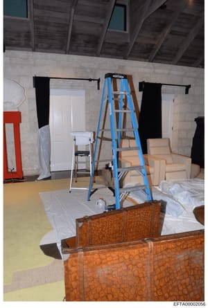 This is an evidence photograph showing an interior room under renovation or construction, featuring exposed concrete walls, wooden beam ceiling, and various construction equipment and furnishings covered with protective plastic sheeting. The image do