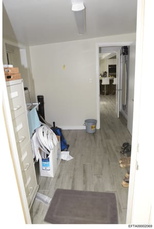 This is an evidence photograph showing the interior of a utility or laundry room in what appears to be a residential property. The room contains a washer/dryer unit, storage shelving, cleaning supplies, and miscellaneous household items. The photogra