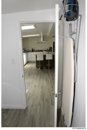 This is an evidence photograph showing the interior of a residential property, specifically a hallway/entryway with a view into a modern kitchen area. The image captures white cabinetry, bar seating, wood-look flooring, and various household items. T
