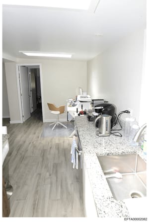 This is a photograph of a contemporary kitchen and adjacent office area, showing granite countertops, stainless steel appliances, modern furniture, and office equipment. The image appears to be documentation of an interior space, possibly from a resi