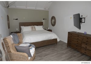 This is a photograph of a furnished bedroom interior, likely from one of Jeffrey Epstein's properties. The room features a wooden bed frame, matching wooden dresser, wicker chair, and coastal-themed decorative elements. The image appears to be eviden