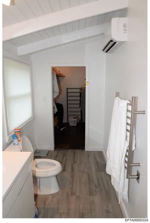 This photograph documents the interior of a bathroom facility featuring a toilet, sink, towel warming rack, and an adjacent storage closet. The image appears to be evidence documentation from a property investigation, showing the layout and condition