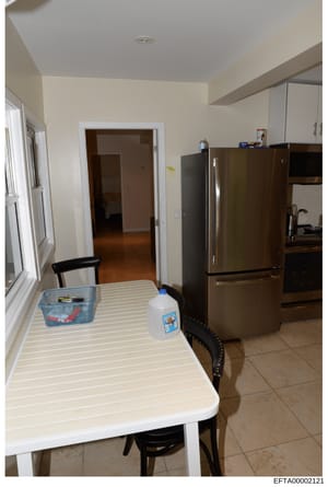 This is a photograph of a kitchen interior showing appliances, dining furniture, and general layout. The image appears to be from property documentation or evidence collection, showing a residential kitchen space with contemporary furnishings and equ
