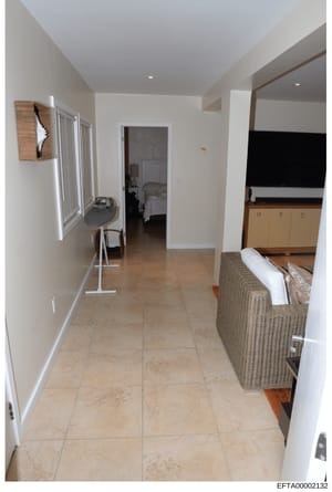 This is a documentary photograph of an interior residential space, showing a master bedroom suite with an attached ensuite bathroom. The image captures a spacious, modern room with beige tile flooring, white walls, and contemporary furnishings includ