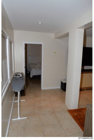 This is a photograph of an interior hallway or entryway of a residential property, showing tile flooring, white walls, an open doorway to a bedroom, and various household items. The image appears to be part of property documentation, possibly related