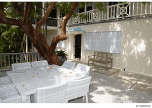This photograph shows an outdoor patio area of one of Jeffrey Epstein's properties, featuring white wicker seating, mature trees, and architectural elements including railings and a second-story balcony. The image appears to be evidence documentation