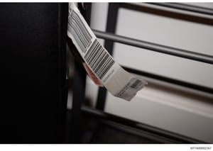 This is a photograph of a physical evidence item bearing multiple barcodes and identification labels, likely taken during the evidence documentation and cataloging process. The item appears to be a cylindrical object with a white label containing bar