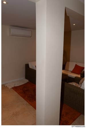 This is an evidence photograph showing the interior of a residential space, likely a bedroom or guest room, featuring two separate sleeping areas divided by a central white column. The room contains dark wicker or rattan furnishings with white and re