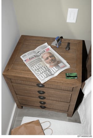 This is an evidence photograph showing a wooden nightstand with multiple drawers in what appears to be a bedroom. On top of the nightstand are a New York Post newspaper with a headline about Jeffrey Epstein, a digital device (possibly a tablet or rea