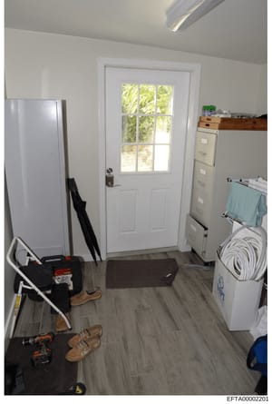This is a photograph of an interior room, likely a utility room, garage area, or storage space. The room contains various tools, equipment, and household items including a refrigerator, filing cabinets, power tools, shoes, and coiled cables. The spac