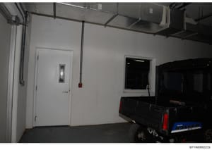 This is a photograph of an interior garage or storage facility showing a white-walled room with industrial features. A Polaris Ranger vehicle is visible on the right side of the image. The space appears to be part of a property associated with the in