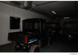 This photograph shows the interior of a garage or storage facility containing multiple dark-colored vehicles, including what appears to be a Range Rover (visible blue nameplate) in the foreground. The facility features industrial ceiling fixtures, fl