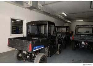 Photograph showing the interior of a garage or storage facility containing multiple utility vehicles, including a Polaris Ranger UTV and other similar off-road equipment. This appears to be an evidence photo from the investigation documenting assets 
