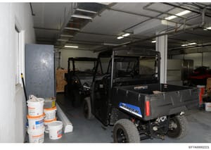 This photograph shows an interior storage garage or warehouse space containing multiple vehicles, including what appears to be utility vehicles and a Ford Ranger pickup truck, along with various stored supplies and buckets. The image documents the co