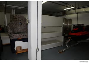 This is an evidence photograph showing the interior of a large storage facility or warehouse space. The image depicts various items in storage including a decorative woven chair, a red jet ski, white shelving units, and other recreational equipment. 