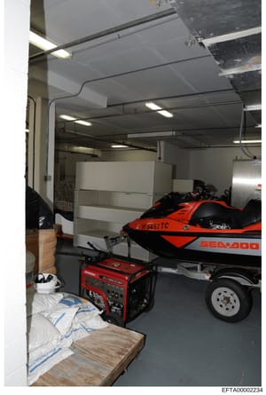 This photograph shows the interior of a storage garage or warehouse space containing recreational watercraft and power equipment. A red and black Sea-Doo jet ski (registration VI 5452 TC) is visible on a trailer, along with a red Honda generator, bui