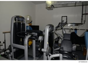 This photograph shows the interior of a gymnasium or fitness facility containing multiple pieces of exercise equipment including weight machines, an exercise bike, and treadmill-style equipment. The image appears to be from an evidence collection rel
