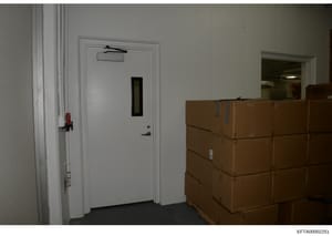 This photograph shows an interior storage or utility room containing multiple stacked cardboard boxes and a fire extinguisher mounted on the wall. The image appears to be evidence documentation from the investigation, showing the physical condition a