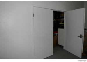 This photograph shows an interior space featuring two white double doors in an open position, revealing a darkened room or storage area with various items visible inside. The image appears to be documentation of a property's interior layout, potentia