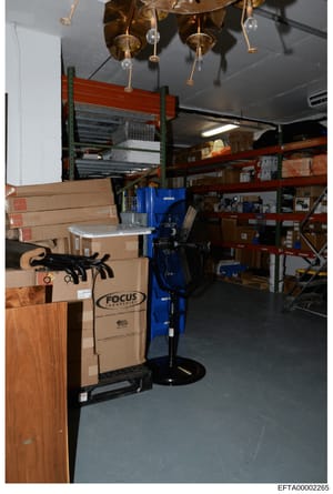 This is a photograph of an interior storage space containing multiple cardboard boxes, industrial shelving units, and various equipment. A Focus Industries branded box is visible in the foreground. The image appears to be documentation of property co