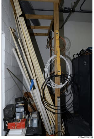 This photograph depicts an interior storage or utility space, likely a basement or closet area, containing building materials, electrical cables, extension cords, and hardware supplies. The image shows wooden ladder segments leaning against a wall, v