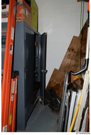 This photograph shows an interior storage or utility area containing a large dark-colored refrigerator, an orange ladder, wooden boards leaning against a white brick wall, and various tools and equipment. The image appears to be part of evidence docu