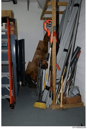 This is an evidence photograph showing the interior of a storage space containing various tools and equipment including ladders, a bicycle, sheets of metal or drywall, and other miscellaneous items. The photograph was taken as part of the investigati
