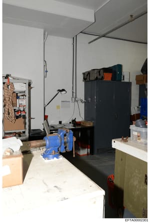 This is an evidence photograph of a basement or workshop area containing tools, equipment, and storage items. The space shows a work bench, tool storage, a blue vise, hanging rope, and various containers and supplies. The photograph appears to be par