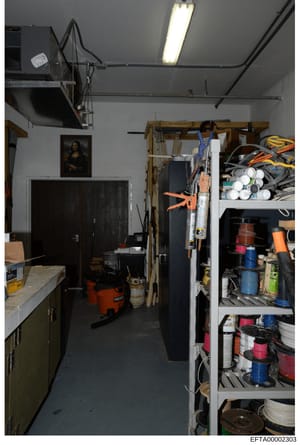 This is an interior photograph of a storage or workshop space containing tools, supplies, and miscellaneous items organized on shelves and hanging storage. The room features utility shelving, an orange power tool (wet/dry vacuum), paint cans, tools, 