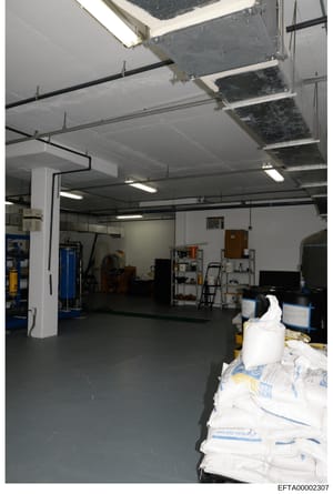 This is an evidence photograph showing the interior of what appears to be a garage or storage space. The image depicts a large, well-lit industrial space with concrete flooring, white support columns, exposed ceiling infrastructure, and various store