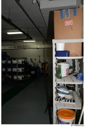 This is an evidence photograph showing an interior storage or utility room containing industrial shelving units, various containers, tools, and household supplies. A large cardboard box marked 'FRAGILE' is visible on upper shelving. The room appears 