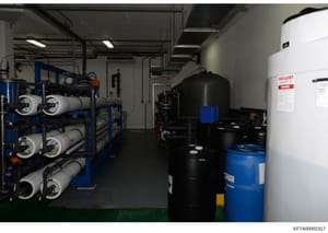 This photograph shows an industrial or commercial mechanical room, likely part of an Epstein property, containing water filtration and treatment equipment including multiple filter vessels, storage tanks, and plumbing infrastructure. The image docume