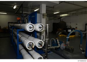 This photograph shows an industrial facility containing large-scale water treatment or filtration equipment, including multiple cylindrical filter vessels with pressure gauges, piping systems, and auxiliary equipment. The image appears to be document