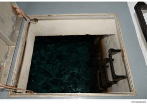 This photograph shows an overhead view of what appears to be a water tank or cistern aboard a vessel, with dark water visible inside and rusty metal fixtures and hardware visible on the white-painted interior walls and rim. The image is likely docume
