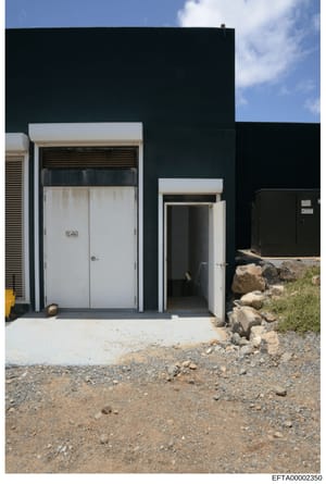 This is an evidence photograph showing the exterior of a modern building structure with a distinctive dark facade, white-trimmed doorways, and metal roller shutters. The image captures two entrance doors and appears to be documentation of a property 