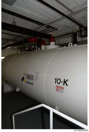 This is a photograph of a commercial fuel storage tank inside an industrial building or facility. The tank is labeled '10-K' and displays warning labels for diesel fuel and flammable materials. The image shows the tank's exterior, overhead piping inf