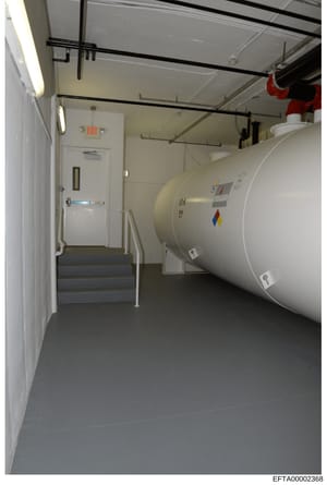 This photograph documents an underground mechanical room or utility space, likely in a building associated with the investigation. The image shows a large cylindrical storage tank (possibly for fuel, water, or other materials) alongside utility infra