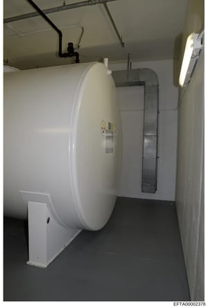 This is an evidence photograph showing the interior of a utility or storage room containing a large white cylindrical tank with plumbing connections and associated piping infrastructure. The image appears to be from a property inspection or inventory