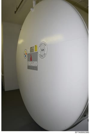 This photograph shows a large white cylindrical storage tank, likely used for water or chemical storage, located indoors. The tank bears manufacturer labels from Highland Tank Manufacturing Company and other regulatory or safety markings. The image a