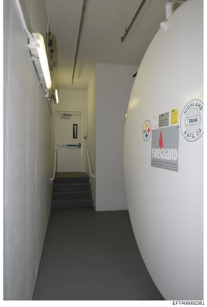 This is an evidence photograph depicting an interior hallway or utility corridor, likely from one of Epstein's properties. The image shows a narrow hallway with fluorescent lighting, white walls, a dark floor, and visible industrial equipment includi