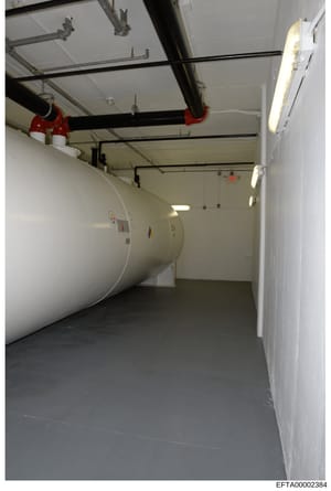This is a photograph of an interior mechanical or utility room, likely from a residential or commercial property associated with the investigation. The image shows HVAC equipment, including large cylindrical tanks with colored bands (red and yellow m