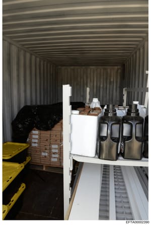 This photograph documents the interior of a storage container containing various seized items including packaged materials, stainless steel containers, and wooden crates with labeling. The image appears to be evidence documentation from a property se